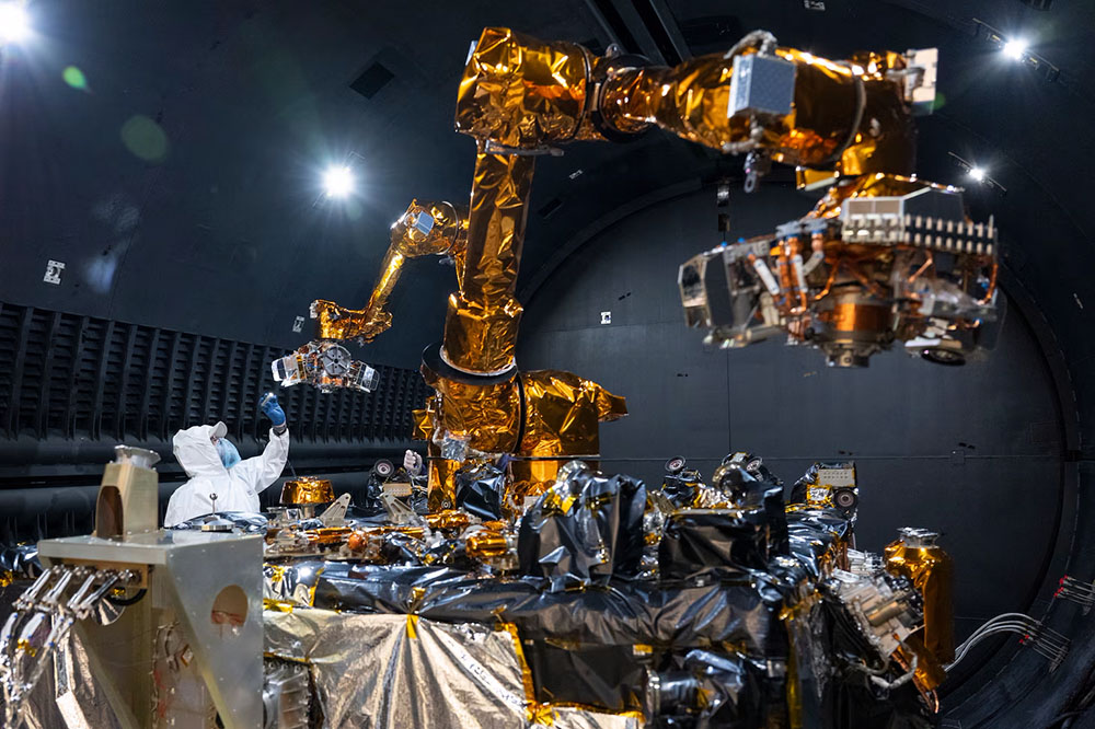 Steven Butcher, Technology Service Corporation space robotics and mechanisms engineer, performs an inspection of the Robotic Servicing of Geosynchronous Satellites (RSGS) payload after completing testing in the cryogenic thermal vacuum chamber. The system is made up of two, long, golden robotic arms.