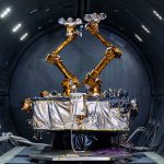 The Robotic Servicing of Geosynchronous Satellites (RSGS) payload, two gold robotic arms inside a grey tunnel.