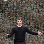 Man in black shirt stands in front of screen displaying thousands of small images