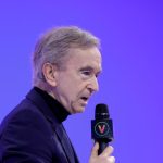 Man in black shirt speaks into mic against purple background