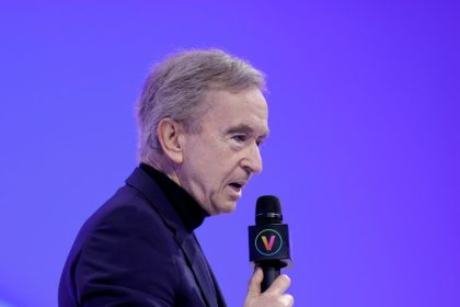 Man in black shirt speaks into mic against purple background