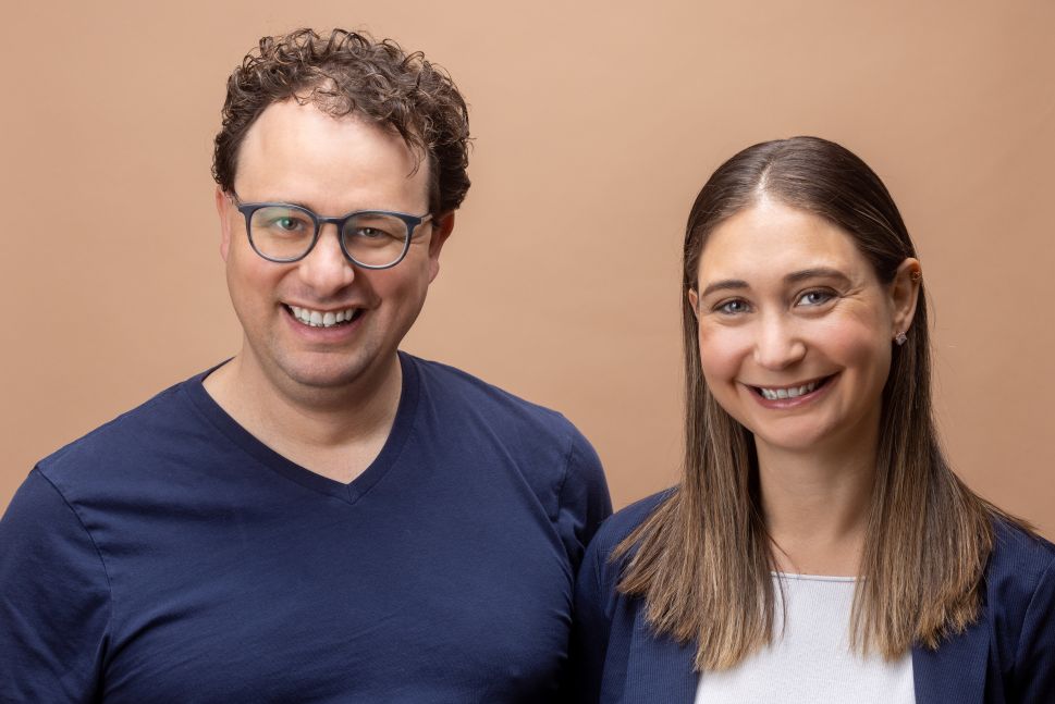 Man and woman pose behind light orange wall