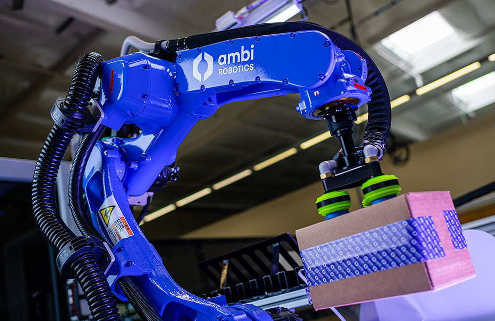 Ambi Robotics 的 AmbiSort A 系列机器人正在抓取一个带有紫色灯光的纸板箱。