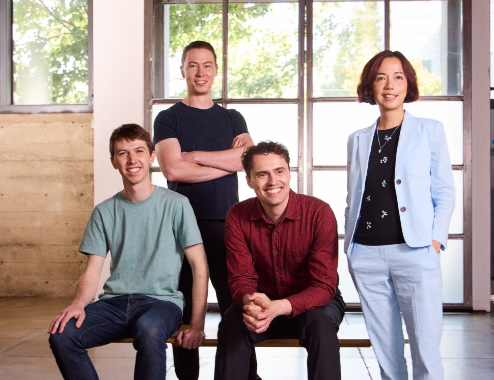 Three men and one woman pose in front of large window