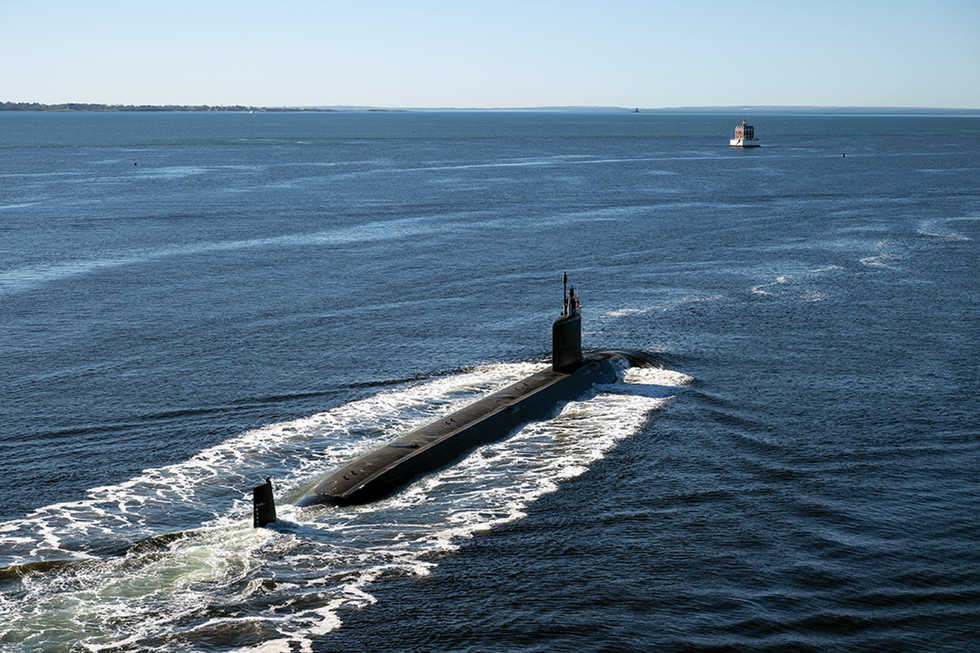 Photo of a half-submerged submarine in the ocean with a visible wake.