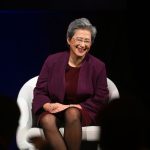 Woman in burgundy blazer suits in white chair onstage