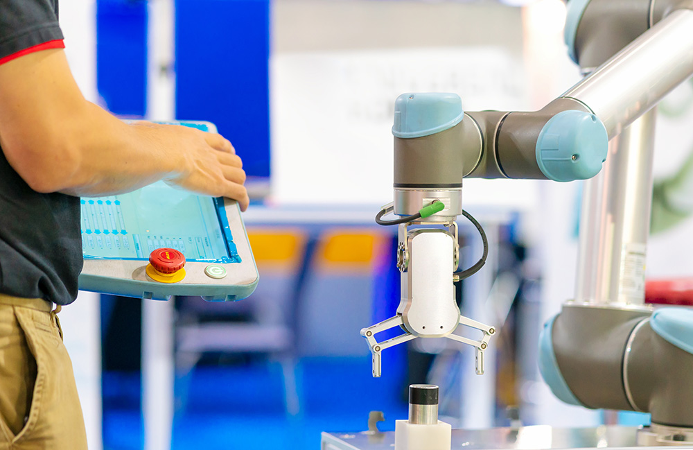 A cobot arm about to pick up an item next to a person holding a tablet. Collaborative robot sales should rebound, according to ABI Research.