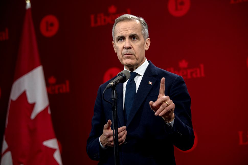 Man in black suit stands at microphone stand in front of red background