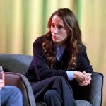 一位身着黑色套装的女性坐在舞台上的椅子上