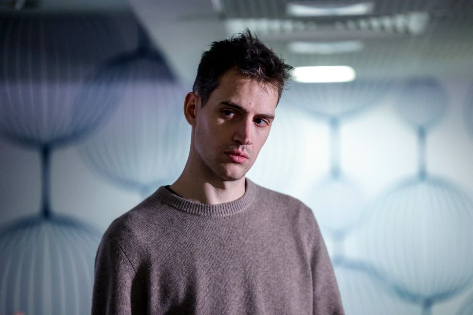 身着米色毛衣的男子站在白墙前