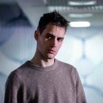 身着米色毛衣的男子站在白墙前