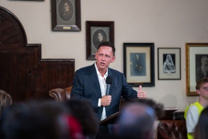 西装男子坐在椅子上对着麦克风讲话